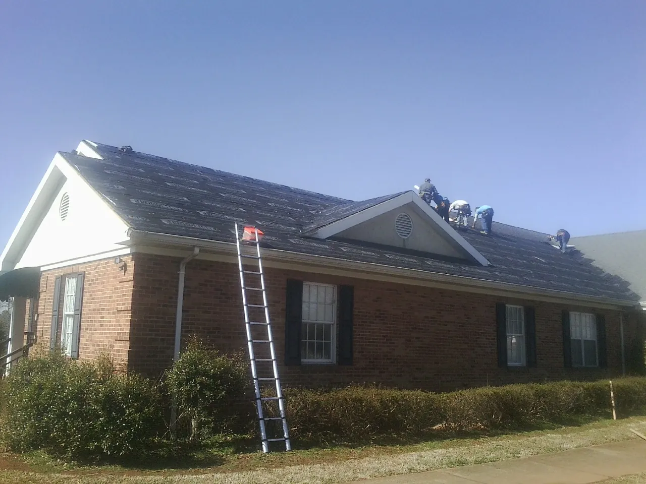 Crew tearing shingles off a brick ranch roof with a ladder set — Metal Roof Repair work by our crew in Saint Ansgar