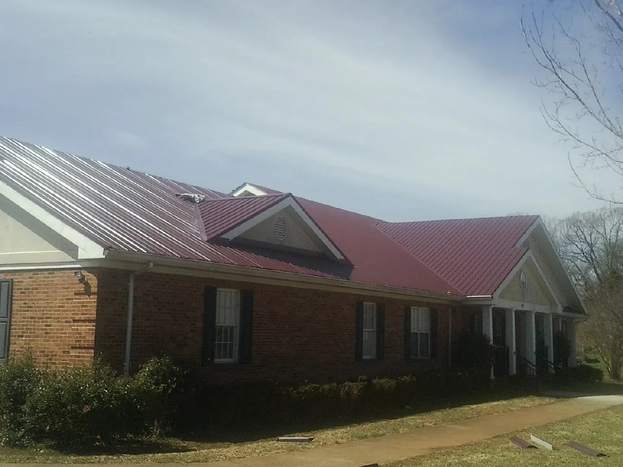 Red metal roof with gabled entries on a long brick building, from a Hail Damage Roof Repair job in Saint Ansgar