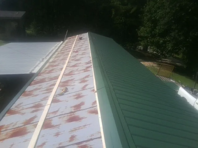 Old rusted panels beside newly installed green metal roofing — Wind Damage Roof Repair by Roofing Brothers in Saint Ansgar