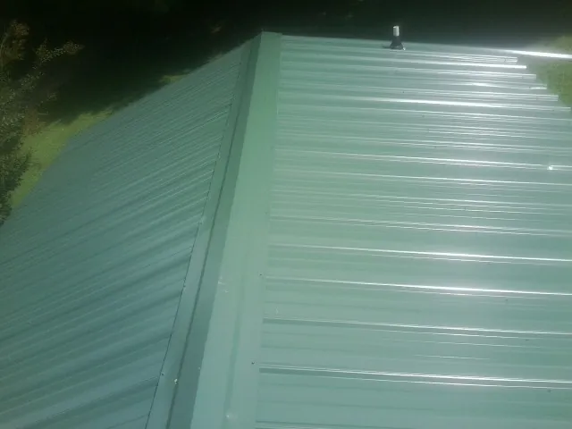 New green metal panels meeting at the ridge of a roof — Flat Roof Repair work by our crew in Saint Ansgar