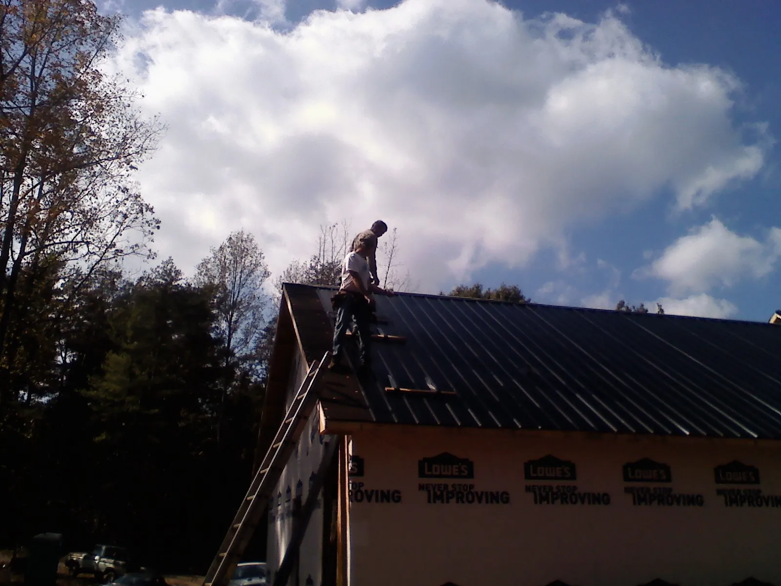 Roofer fastening dark metal panels high against a cloudy sky, from a Roof Inspection job in Saint Ansgar