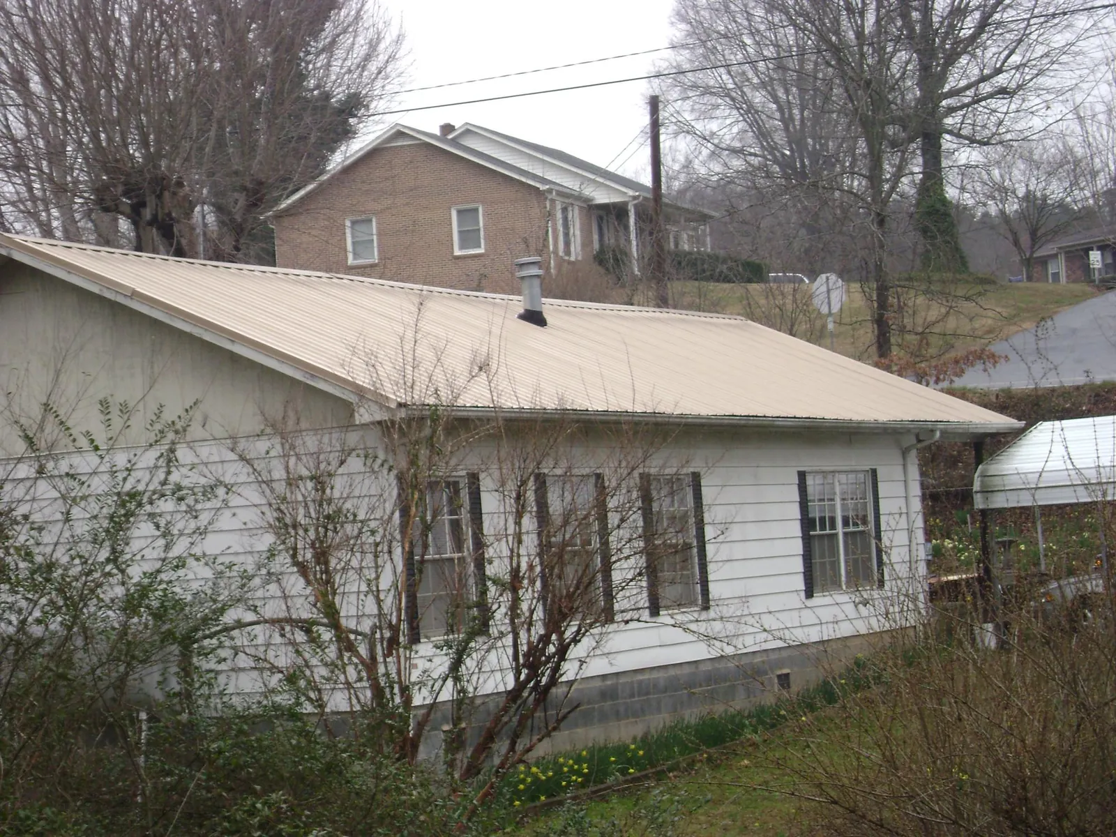 Tan metal roof on a white sided house set into a hillside — Commercial Roofing by Roofing Brothers in Saint Ansgar