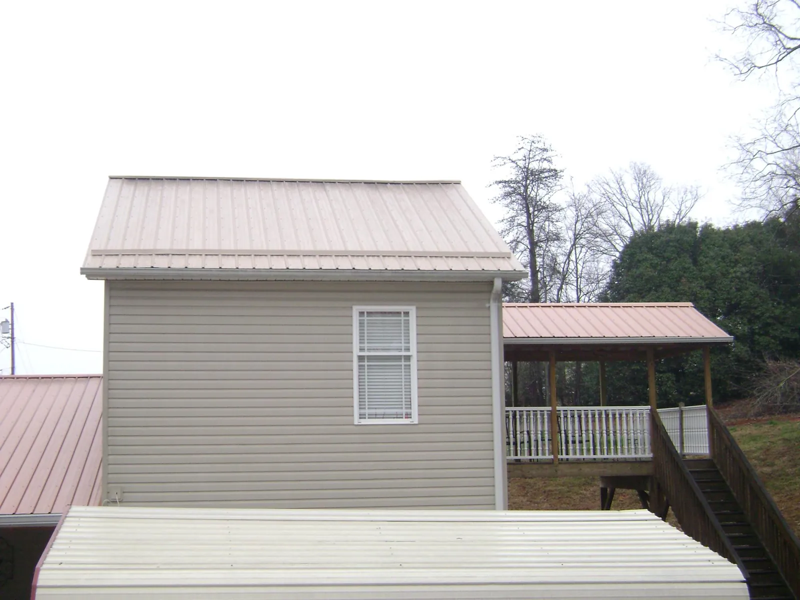 Tan metal roofs on a two story addition and attached porch, from a Roof Replacement job in Saint Ansgar