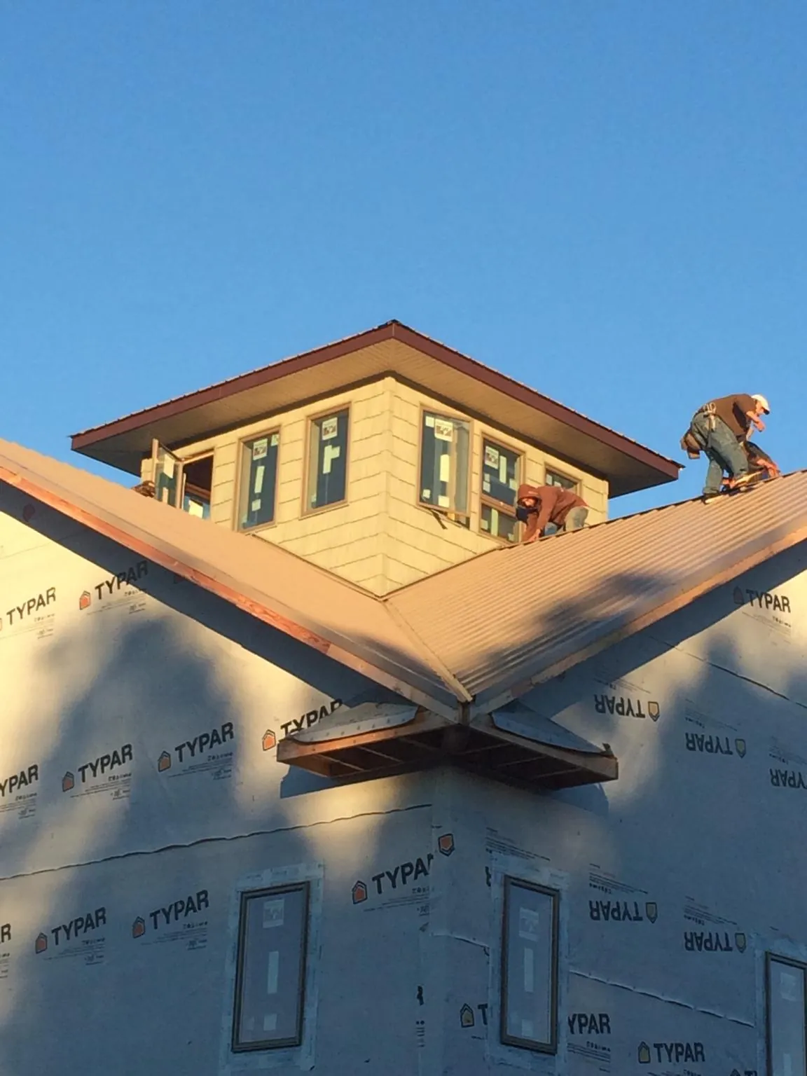 Roofers working around a rooftop cupola on a new metal roof at sunset in Saint Ansgar